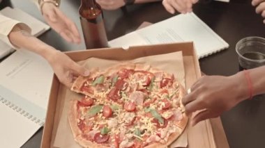 Konferans salonundaki kutudan pizza parçalarını alan tanınmayan insanların yüksek açılı elleri.