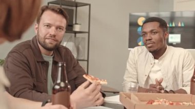 İş toplantısından sonra masa başında oturan, pizza yiyen, bira şişelerini tıkırdatan ve içki içen beyaz ve Afrikalı erkeklerin belden yumağı.