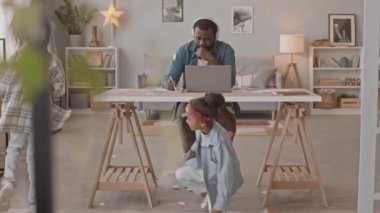 Kafasına ve kıyafetlerine yapışkan notlar takmış, iki küçük kızı yaramazlık yaparken ve dikkat dağıtırken Afrikalı Amerikalı adamın yavaş çekimleri.