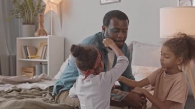 İki küçük Afro-Amerikalı kızın, babalarının evde birlikte eğlenirken yüzüne makyaj yaparken orta yavaş çekimleri.