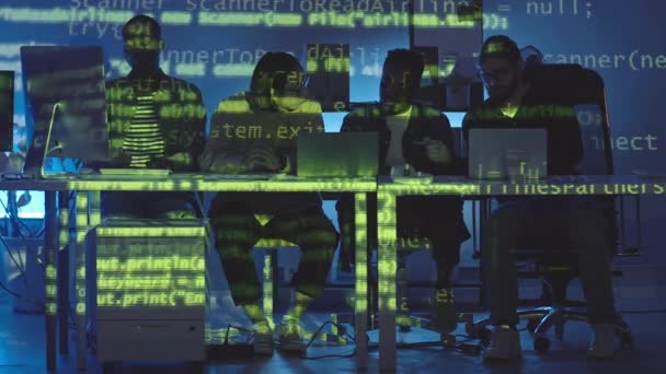 夜暗いオフィスで働く4人の若い多民族のプログラマーに投影緑のプログラミングコードを実行しているスタブショット — ストック動画