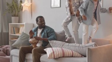 Rahat oturma odasındaki kanepede zıplayan ve babaları yakınlarda Afrika davulu çalarken iki küçük tatlı kızın yavaş çekimleri.