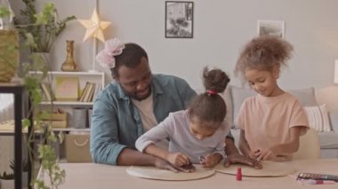 İki küçük kız kardeşin, sevgili babalarının tırnaklarını ojelerken, rahat oturma odasında pembe kurdeleyle otururken orta yavaş çekimleri.