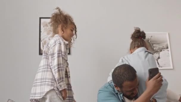 慢镜头拍摄的快乐的非裔美国男人和他的两个可爱的漂亮女儿一起在舒适的公寓沙发上玩乐 女孩们想爬上她们的爸爸的肩膀 — 图库视频影像
