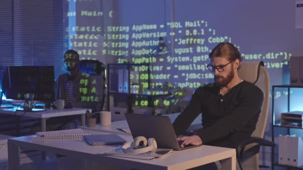 两名不同的男性程序员坐在黑暗办公室的工作场所 在办公室内部投射正在运行的程序代码 — 图库视频影像