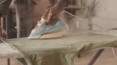 Evdeki ütü masasında tişörtünü ütüleyen, Afrika kökenli tanınmayan bir adamın yakın çekimi.