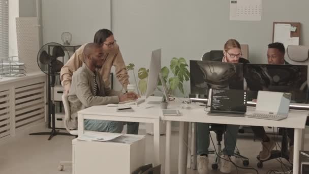 現代のオフィスでチームで働く多様な民族の4人の若い男性プログラマーのパンニングショット キーボードを入力し コンピュータモニタの前で話す — ストック動画