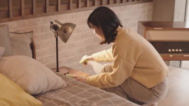 Asyalı ev kadınlarının yavaş çekimleri komodinin üzerinde lambaları ilaçlıyor ve yatak odasını temizliyor.