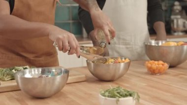 Taze sebze salatasını kasede karıştıran önlük giymiş, baharat olarak sebze yağı getiren, profesyonel mutfakta yemek pişiren bir aşçı yamağı.