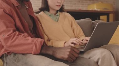 Modern evlerindeki koltukta oturan, dizüstü bilgisayarlarına bakıp gülen mutlu, çoklu etnik kökenli çiftin yavaş çekimleri.