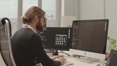 Ciddi bir programcının belden aşağısı, sakallı bir programcının modern açık uzay ofisinde iş arkadaşlarıyla otururken bilgisayardaki yazım kodunu gösteriyor.