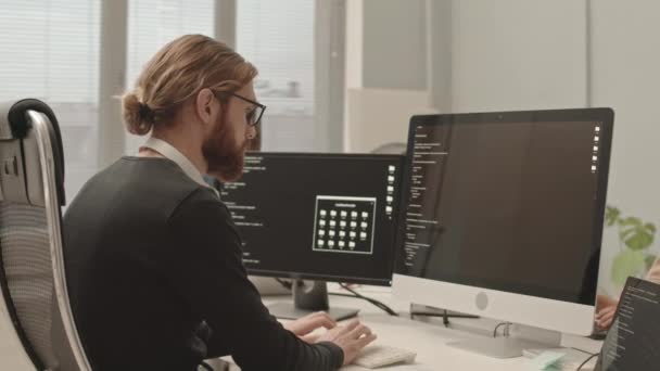 ハンドヘルド腰アップアップ遅いショットの深刻なプログラマーとともに髭のタイピングプログラムコード上のコンピュータ座っています現代的なオープンスペースオフィスで同僚と — ストック動画