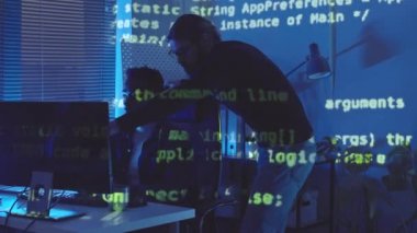 Ofisin içini gösteren programlama kodları ve geceleri bilgisayarda çalışan iki genç erkek programcı.
