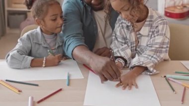 Orta boy, mutlu, Afro-Amerikan bir adamın iki tatlı kızıyla birlikte vakit geçirip rahat evinde resim çizerken ve eğlenirken çekilmiş bir fotoğrafı.