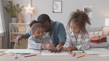 İki küçük kız kardeşin, babalarıyla rahat bir evde vakit geçirip avucunun içinde kağıt parçalarıyla eğlenirken orta boy, yavaş çekimleri.