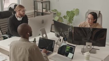Modern ofiste bilgisayarların başında oturan üç farklı erkek programcının yavaş çekimi.