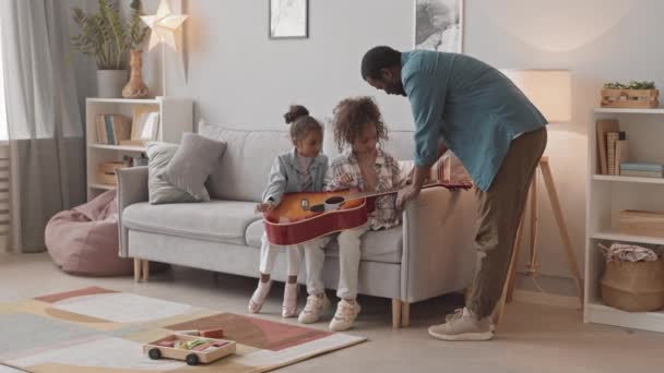 慢镜头拍摄的非裔美国人和他的两个可爱的小女儿在舒适的客厅沙发上弹奏吉他 他们在一起玩得很开心 — 图库视频影像