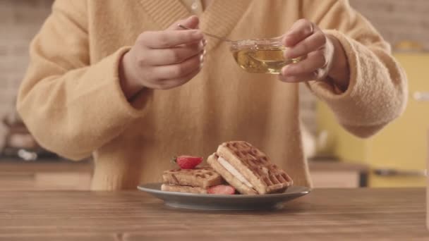 身着黄色针织衫的女人在中段慢吞吞地把蜂蜜倒在美味的草莓松饼上 — 图库视频影像