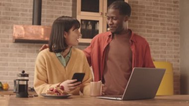 Evde kahvaltı ederken, laptopta arkadaşlarıyla sohbet eden mutlu, çoklu etnik çiftlerin orta yavaş çekimleri.