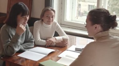 Orta yavaş çekimde, çok ırklı üniversite arkadaşları masada oturmuş sohbet ediyorlar.