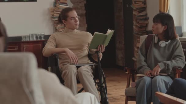 障害者読書本を持つ白人男性学生の手によるスローショット大学で文学クラブ会議中に一緒に円に座ってクラスメートの前で — ストック動画