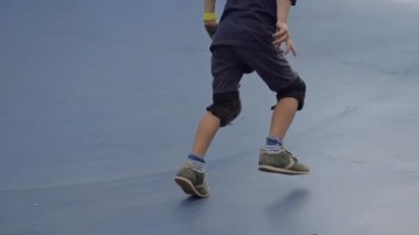 Diz ve dirsek yastıklarından kayarak kayan 7 yaşındaki beyaz bir çocuğun açık hava çocuk parkındaki kaykay pistindeki görüntülerini izliyoruz.