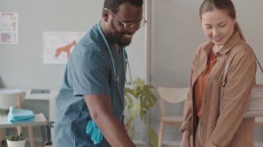 Genç siyah veteriner önlük ve gözlük takmış, gündüz vakti klinikte konuşan ve gülümseyen beyaz kadın Labrador köpek sahibini selamlıyor.