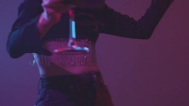 Süslü siyah uzun kollu beyaz bir kadının neon ışıklı bir partide kırmızı şarap kadehiyle dans edişinin yavaş çekimini kaldır.
