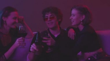 İki güzel kızın modaya uygun kırmızı güneş gözlüklü bir adamla flört ettiği, içki içtiği ve gece kulübündeki kanepede oturup sohbet ettiği belden aşağı vuruşlar.