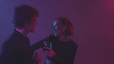 Gece kulübünde mor ışıkta dans eden neşeli, genç beyaz çiftin belini kaldır.