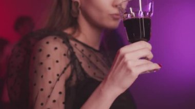 Siyah şeffaf polka örgü tişörtlü, neon ışıklardaki partide bir bardak kırmızı şarapla baştan çıkarıcı bir şekilde dans eden genç ve güzel bir bayanla orta boy yakın çekim.