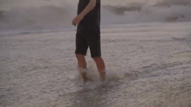 Sıcak bir yaz akşamında deniz kıyısında bacaklarıyla yürüyen küçük bir çocuğun görüntüsü.