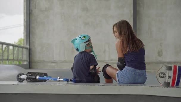 在滑雪场聊天时 白种人活泼的年轻女子和她7岁的儿子都穿着膝盖和肘部垫的后视镜镜头 — 图库视频影像