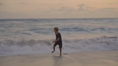 Gün batımında sahilde oynayan, dalgalardan kaçan ve kahkahalarla gülen 7 yaşındaki beyaz çocuğun mutlu görüntülerini çekiyorum.