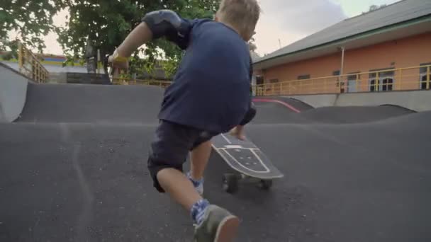 在室外滑板滑板滚下滑板溜冰场后 追踪7岁男孩膝部和肘部推挤和奔跑的镜头 — 图库视频影像