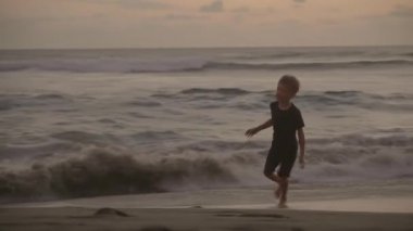 Gün batımında ıssız plajda koşan beyaz bir çocuğun görüntüsü.