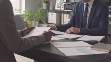 Düşük açılı, resmi takım elbiseli iş adamı sabah ofiste meslektaşının karşısında oturuyor, konuşuyor, belgeleri okuyor, sonra da kalkıp el sıkışıyor.