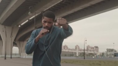 Aktif giyimli ve kulaklıklı bir Afro-Amerikalının soğuk bir sabahta boks antrenmanı sırasında orta yavaş çekimleri.