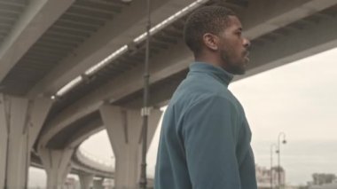 Aktif giyimli, ciddi siyahi bir adamın soğuk bir sabahta dışarıda antrenman yapmadan önce ısınma egzersizleri yaptığı orta boy bir fotoğraf.