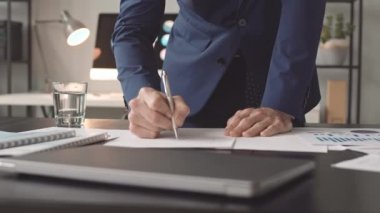 Mavi takım elbiseli, masa başında duran, kağıt üzerinde notlar alan, belgelere bakan düşük açılı erkek CEO.