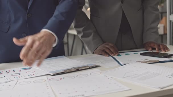 低矮的黑衣人和他的男性同事穿着西装 白天站在办公室的桌子旁 拿着文件 用智能手机 — 图库视频影像