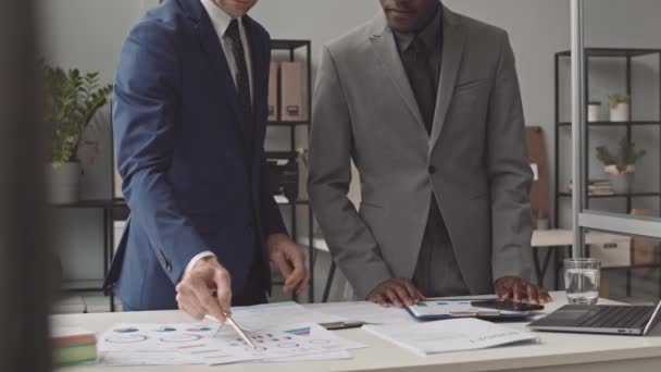中等身材的年轻黑人男子和他的男性同事穿着西装 白天站在办公室的桌子旁 拿着文件 难以辨认 — 图库视频影像