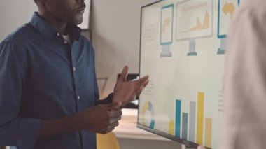 Düşük açılı genç siyah adam ve kırpılmış erkek menajer ekranda sunum ile duruyor, konuşuyor ve planlarını tartışıyorlar.