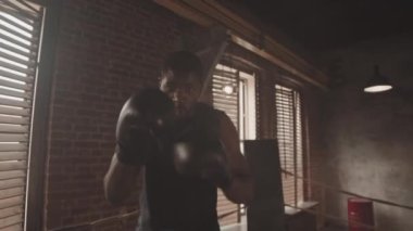 Siyah eldivenli, ağır Afro-Amerikan erkek boksör ağır çekimde. Yumruk atıyor ve ring eğitimi sırasında kameraya bakıyor.