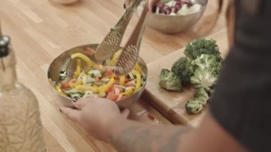 Taze sebze salatasını kabın içinde karıştırıp, sebze yağıyla tatlandırıp, profesyonel mutfakta yemek pişiren yüksek açılı bir aşçı.