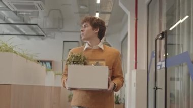 Meslektaşı tarafından hoş karşılandıktan sonra ofis koridorunda elinde karton kutuyla dolaşan beyaz giysili bir gencin orta yavaş çekimini izliyorum.