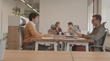 Genç bir adamın iş görüşmesine gelip, özgeçmişini işverenine verirken ve el sıkışırken PAN 'ın yan görüntüsü. Arka plandaki masada sohbet eden iki bayan meslektaşım.