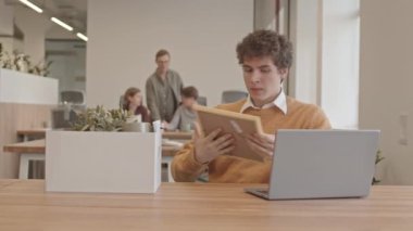 Ofisteki ilk gününde kağıt kutusundan eşyalarını çıkaran ve iş arkadaşına elini sıkan genç adamın yavaş çekimini yapın.