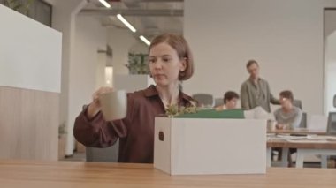 Yeni işyerindeki karton kutusundan eşyalarını boşaltan genç bir kadının orta boy fotoğrafı. Meslektaşım onu el sıkışarak selamlıyor.