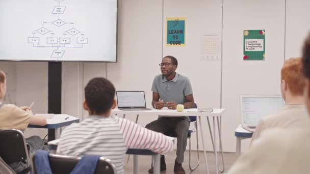 教室の机に座っている若い黒人男性教師の広いショット 授業で認識できない学生を求めて 画面上のプロセスフロー図を指して — ストック動画